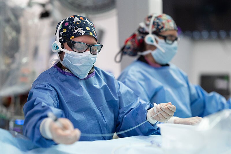 Two surgeons in blue scrubs, masks, and gloves perform a medical procedure in an operating room.