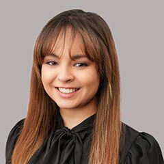 Smiling young woman with long dark hair and bangs in a black blouse.