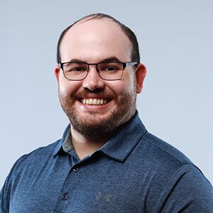 Smiling man with glasses, very short dark hair and beard wearing a blue polo shirt.
