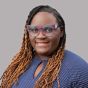 Smiling young woman with glasses and long  ombre braided hair wearing a blue blouse.