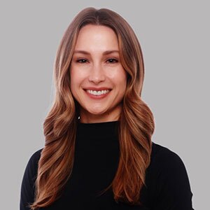 Smiling young woman with long dark blonde wavy hair in black turtle neck.