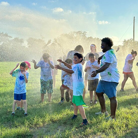 Group of happy children playing in the sprinkler on grass.