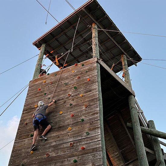 Teenage boy rock climbing a wooden tower.
