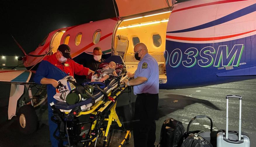 A team of three men loading a baby on a stretcher into a Driscoll fixed-wing aircraft.