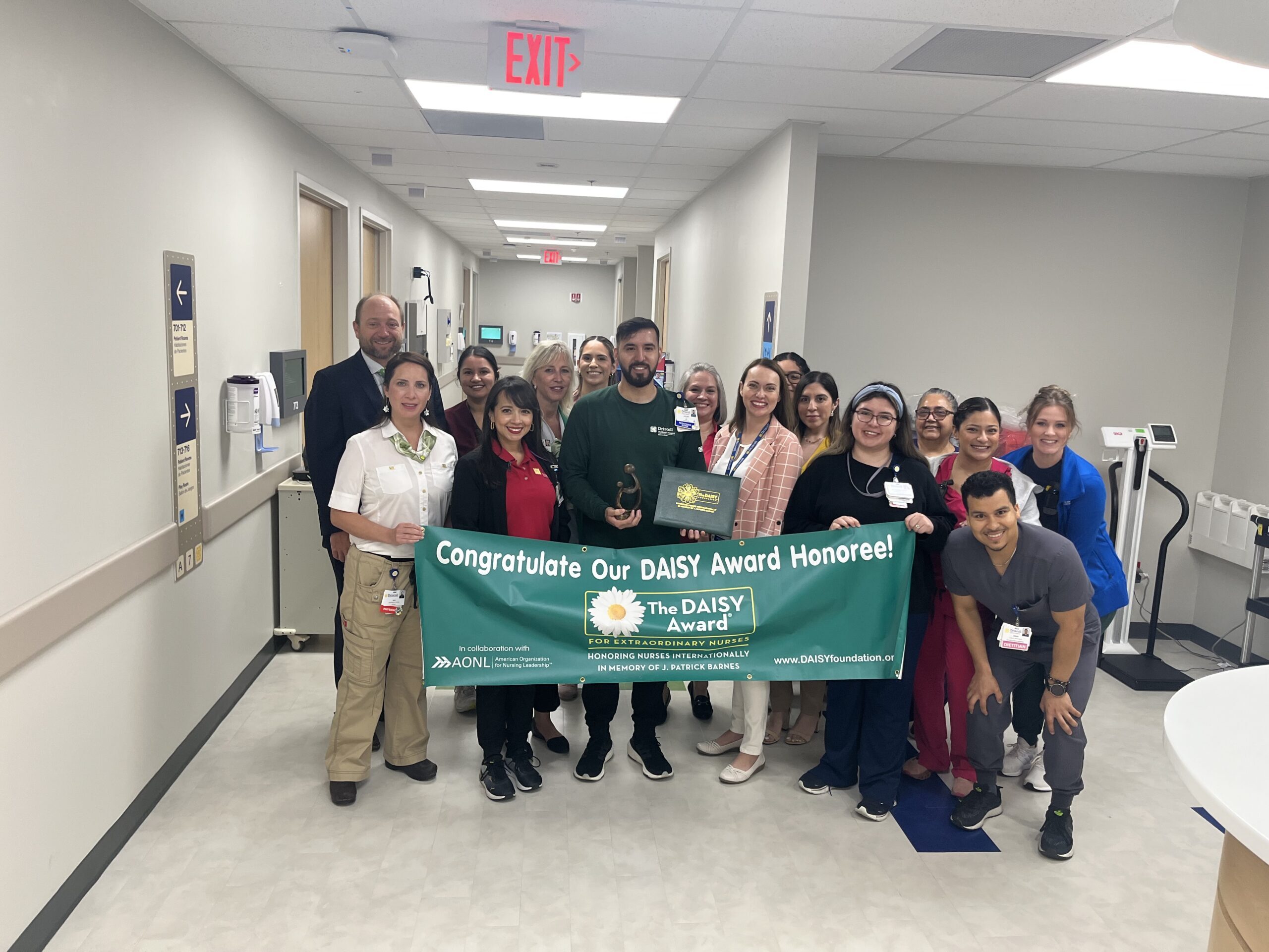 Steff members stand in a hallway holding a banner that says Congratulate our Daisy Award Honoree!