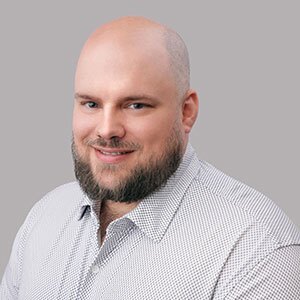 Smiling young bald man with dark beard in white button up collard shirt.