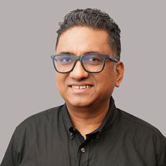 Smiling man with glasses, short black hair wearing a black button up collard shirt.
