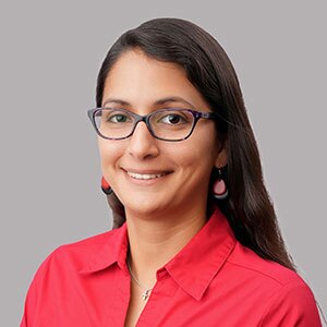 Smiling young woman with glasses and long dark hair wearing a red button up collard shirt.