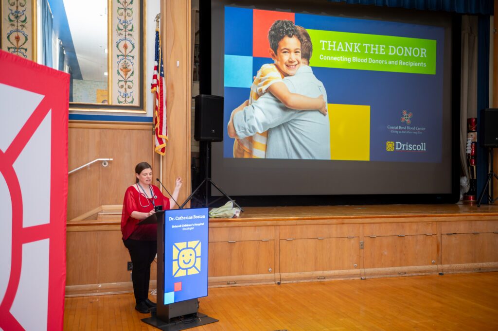Oncologist stands in front of podium in auditorium during event at Driscoll.